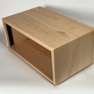 May include: A rectangular wooden box with an open front. The box is made of light-colored wood with visible grain. The interior is a lighter shade of the same wood. The box has a black metal strip on the inside.