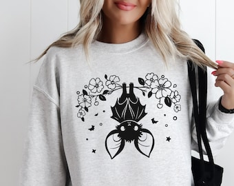 May include: A gray sweatshirt with a black graphic of a bat hanging upside down from a branch with flowers. The bat has large ears and a cute expression.