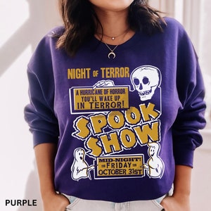 May include: A purple sweatshirt featuring a Halloween design. The graphic includes the words "NIGHT OF TERROR" and "SPOOK SHOW", a skull, and ghosts. The text also reads "MID-NIGHT! = FRIDAY = OCTOBER 31ST".