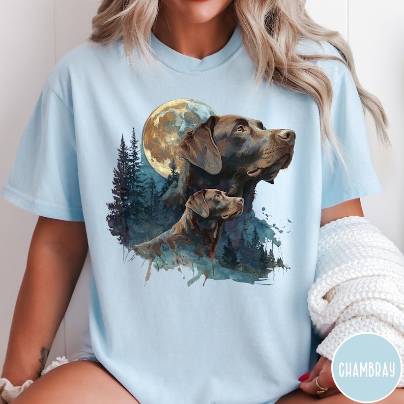 May include: Light blue t-shirt featuring a watercolor illustration of two brown Labrador Retrievers with a full moon and forest background. The design is printed on a soft, comfortable tee, perfect for dog lovers.