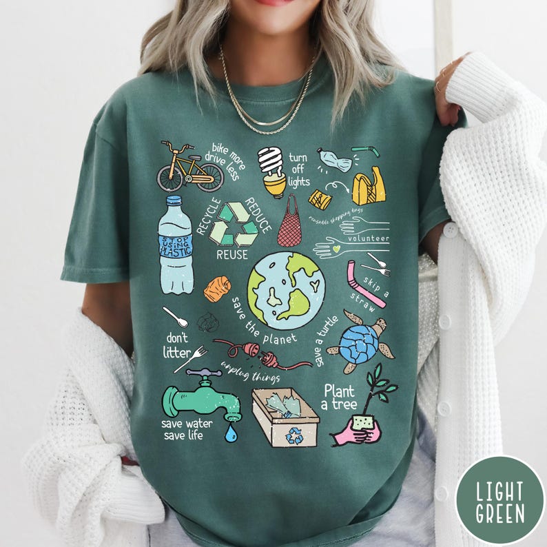 May include: A teal green t-shirt featuring a graphic print of various illustrations related to environmentalism. The illustrations include a bicycle, a water bottle, a globe, a turtle, a plant, and a tap. The text on the shirt includes "bike more drive less", "turn off lights", "reduce", "recycle", "reuse", "volunteer", "skip a straw", "don't litter", "save the planet", "unplug things", "save a turtle", "plant a tree", "save water save life".