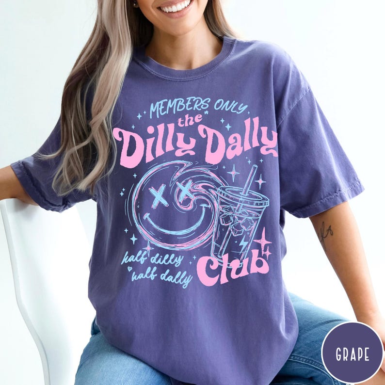 May include: A purple t-shirt with a graphic design featuring the text "MEMBERS ONLY the Dilly Dally Club." The design includes a smiley face, a drink, and the words "half dilly, half dally."