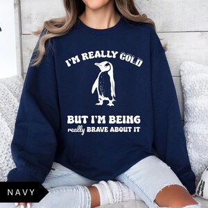 May include: A navy blue sweatshirt with a white penguin graphic and the text "I'm really cold but I'm being really brave about it".