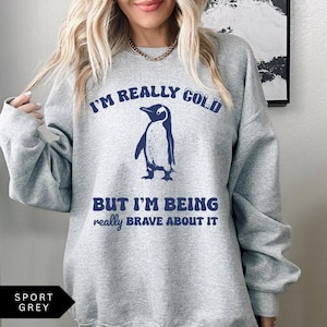 May include: A gray sweatshirt with the text "I'm really cold but I'm being really brave about it" and a cartoon penguin in blue.