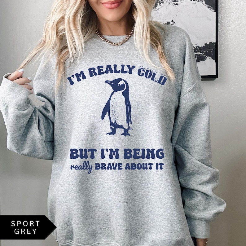 May include: A gray sweatshirt with the text "I'm really cold but I'm being really brave about it" and a cartoon penguin in blue.
