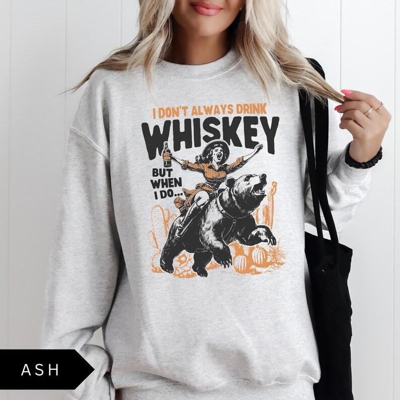 May include: A gray sweatshirt with a graphic print of a woman riding a bear. The text on the graphic reads "I don't always drink whiskey, but when I do..."
