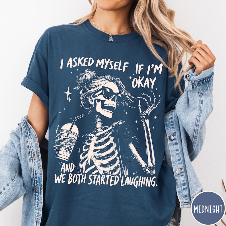 May include: Navy blue t-shirt with a skeleton graphic wearing sunglasses and holding a drink. The text on the shirt reads: "I ASKED MYSELF IF I'M OKAY. AND WE BOTH STARTED LAUGHING."