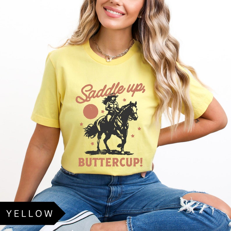 May include: Yellow t-shirt with a graphic of a woman riding a horse and the text "Saddle up, Buttercup!"