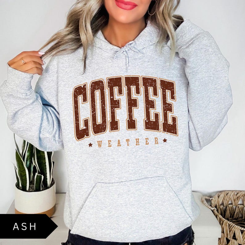 Puede incluir: Una sudadera con capucha gris con un gr&aacute;fico vintage marr&oacute;n que dice "COFFEE WEATHER" en may&uacute;sculas.