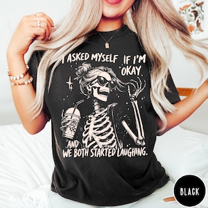 May include: Black t-shirt featuring a skeleton graphic with sunglasses, holding a drink. The text on the shirt reads, "I asked myself if I'm okay. And we both started laughing."