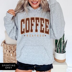 Puede incluir: Una sudadera gris con capucha con un gr&aacute;fico vintage marr&oacute;n que dice "Coffee Weather" en la parte delantera.