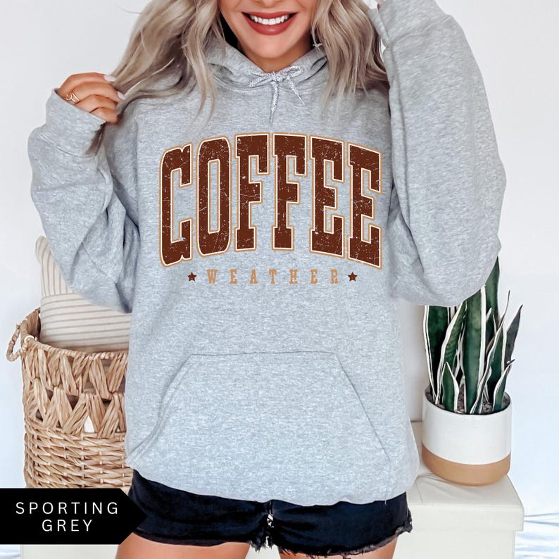 Puede incluir: Una sudadera gris con capucha con un gr&aacute;fico vintage marr&oacute;n que dice "Coffee Weather" en la parte delantera.