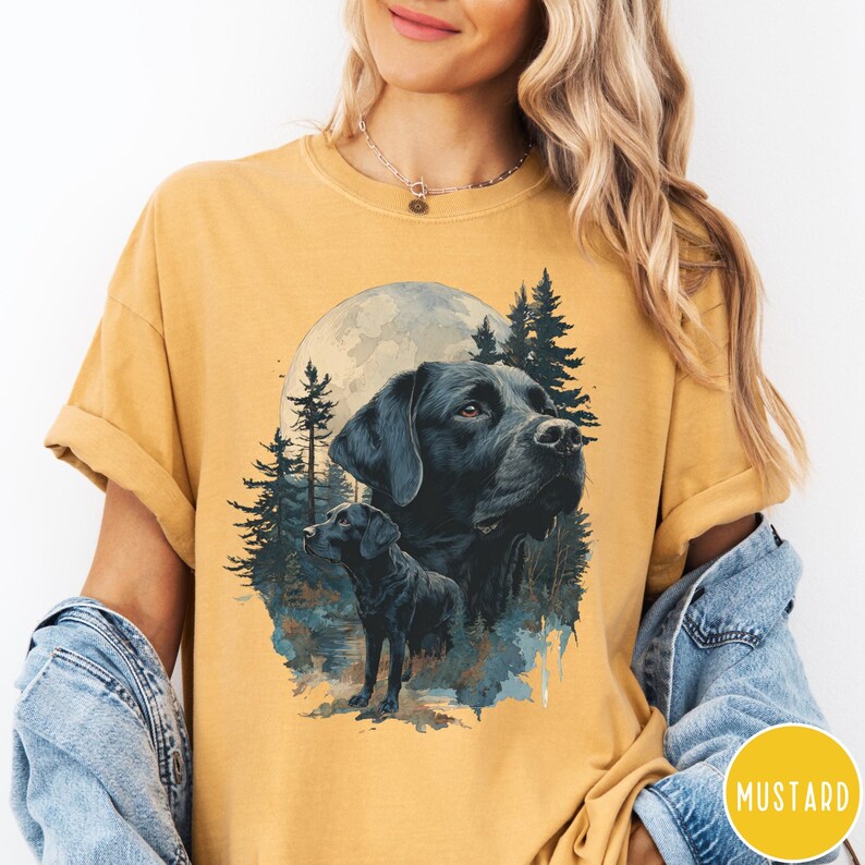May include: Mustard-colored t-shirt featuring a black Labrador Retriever illustration. The design includes a large dog portrait, a smaller dog, a full moon, and pine trees. The word "MUSTARD" is in a yellow circle.