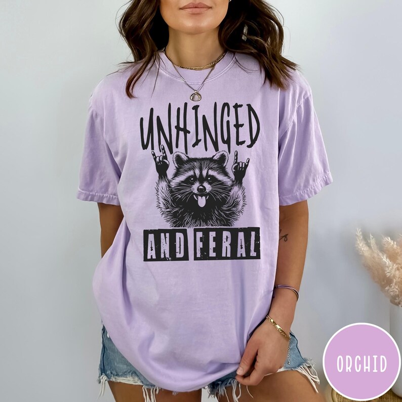 May include: A purple t-shirt with a graphic of a raccoon with the text "Unhinged and Feral".