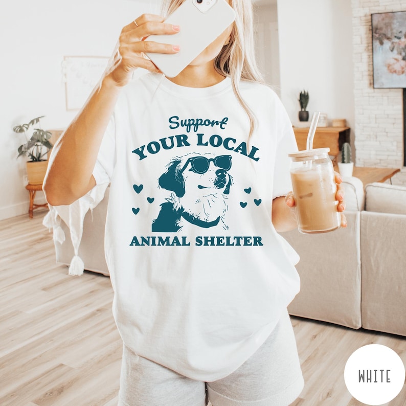 May include: White t-shirt with a blue graphic of a dog wearing sunglasses. The text "Support Your Local Animal Shelter" is printed on the shirt.