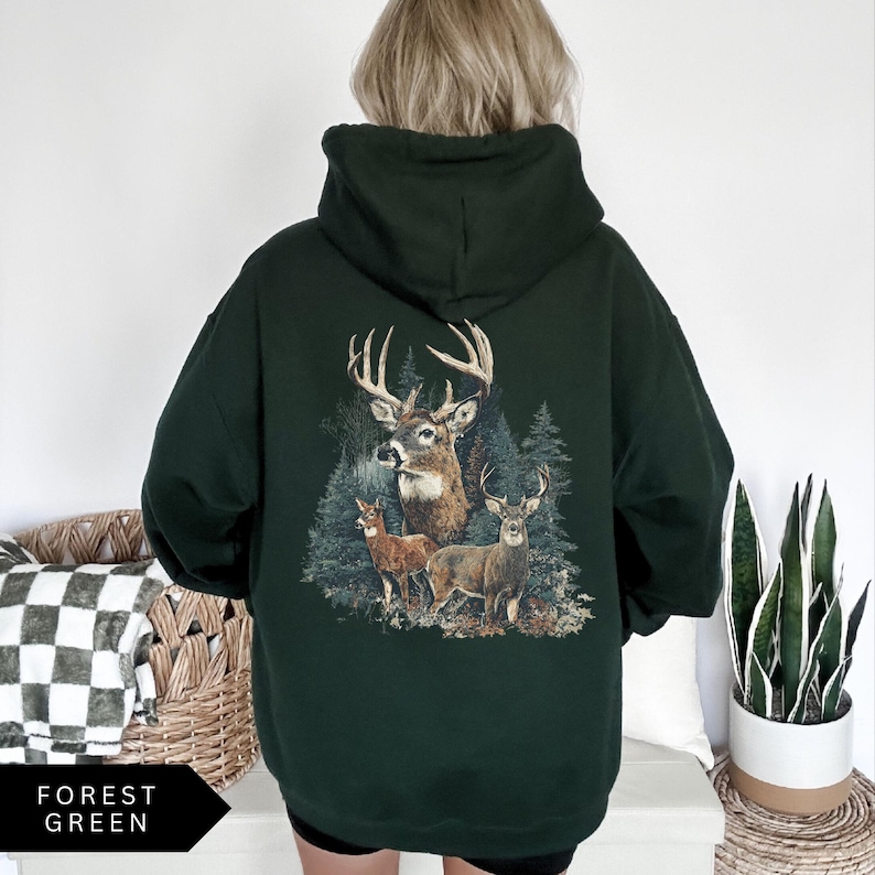 Op de afbeelding: Bosse groene hoodie met een hertenafbeelding op de rug. De afbeelding toont drie herten in een bosrijke omgeving. De hoodie heeft een capuchon en een relaxte pasvorm. De tekst "FOREST GREEN" staat linksonder.