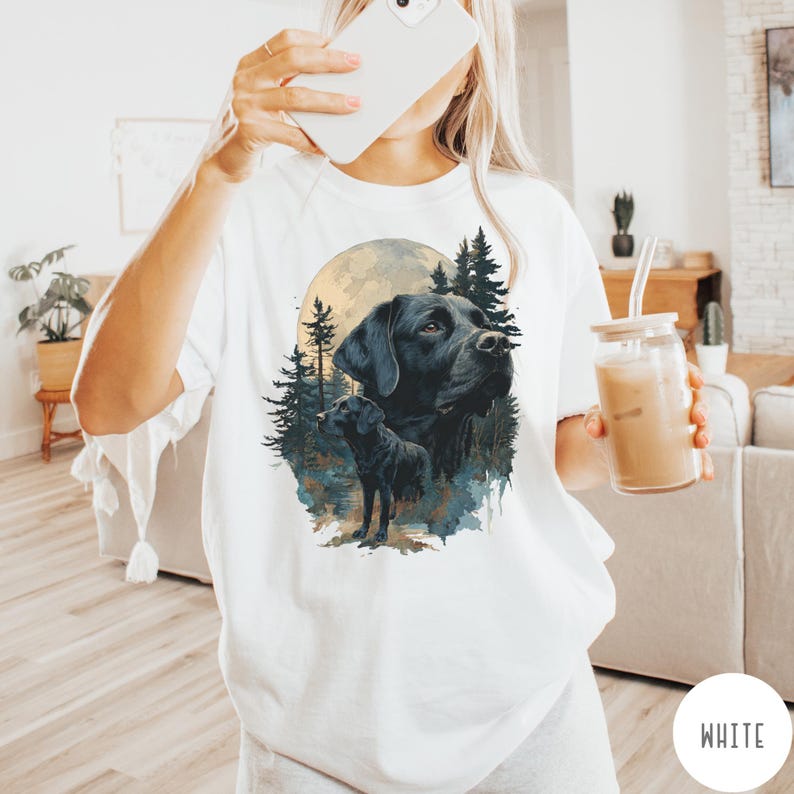 May include: White t-shirt featuring a graphic of a black Labrador Retriever with a full moon and forest background. The design includes a large portrait of the dog and a smaller image of the dog standing. The word "WHITE" is in a white circle.