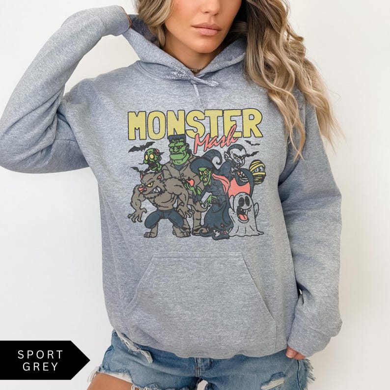Puede incluir: Una sudadera con capucha gris con un estampado gr&aacute;fico de un grupo de monstruos de dibujos animados. El texto "Monster Mash" est&aacute; impreso en amarillo sobre el gr&aacute;fico.