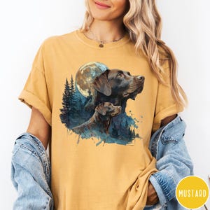 May include: Mustard-colored t-shirt featuring a graphic of two brown Labrador Retrievers under a full moon and a forest silhouette. The design has a watercolor effect. The word "MUSTARD" is in a yellow circle.