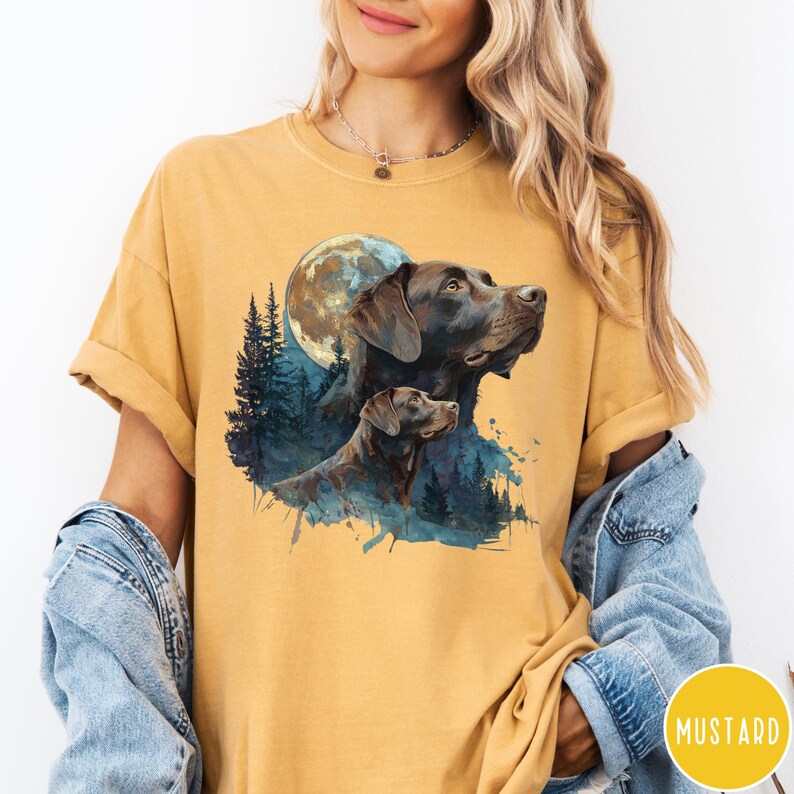 May include: Mustard-colored t-shirt featuring a graphic of two brown Labrador Retrievers under a full moon and a forest silhouette. The design has a watercolor effect. The word "MUSTARD" is in a yellow circle.