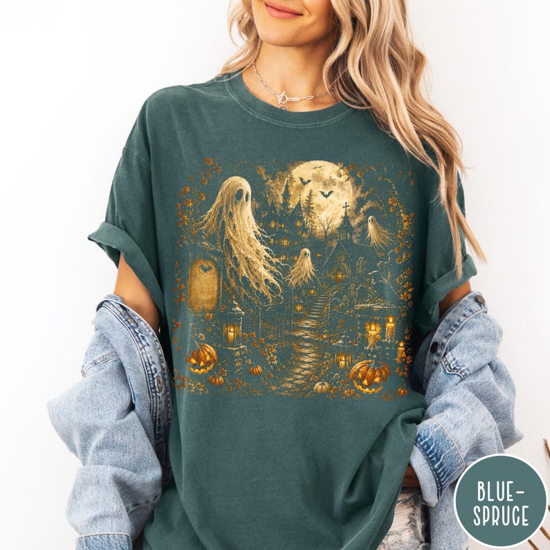 Puede incluir: Una camiseta de manga corta en color verde azulado oscuro con un estampado gr&aacute;fico de una escena embrujada con fantasmas, una luna llena grande, un castillo oscuro y calabazas naranjas, con detalles de un camino y faroles.