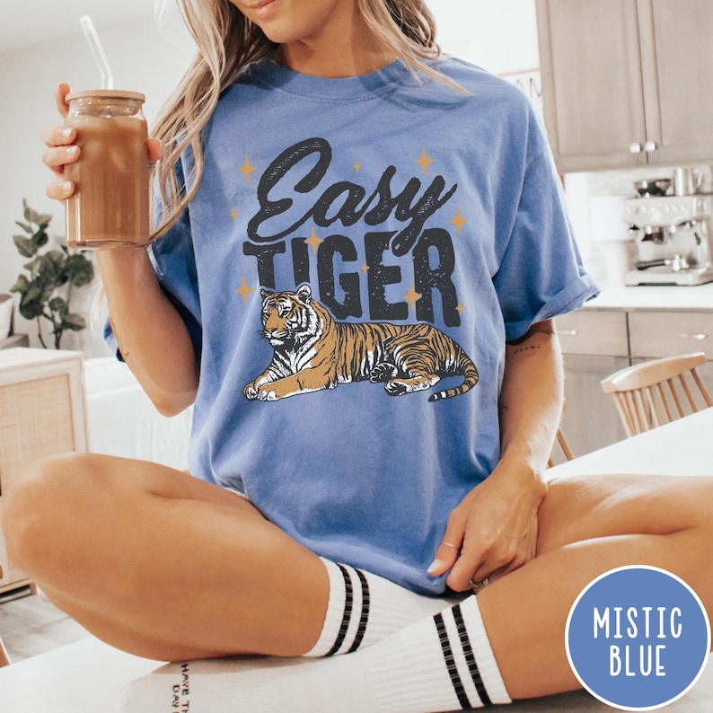 May include: A blue t-shirt with the text "Easy Tiger" in black and a tiger illustration. The shirt has a distressed look and is a relaxed fit.