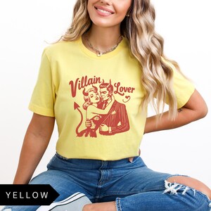 May include: A yellow t-shirt with a red graphic of a couple in a vintage style. The text "Villain Lover" is printed on the shirt.