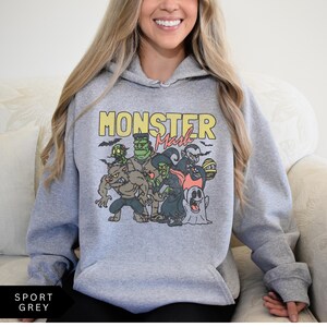 Puede incluir: Una sudadera con capucha gris con un estampado gr&aacute;fico de un grupo de monstruos de dibujos animados. El texto "Monster Mash" est&aacute; impreso en amarillo sobre el gr&aacute;fico.