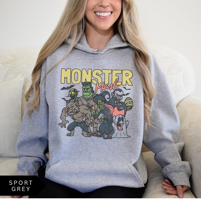 Puede incluir: Una sudadera con capucha gris con un estampado gr&aacute;fico de un grupo de monstruos de dibujos animados. El texto "Monster Mash" est&aacute; impreso en amarillo sobre el gr&aacute;fico.