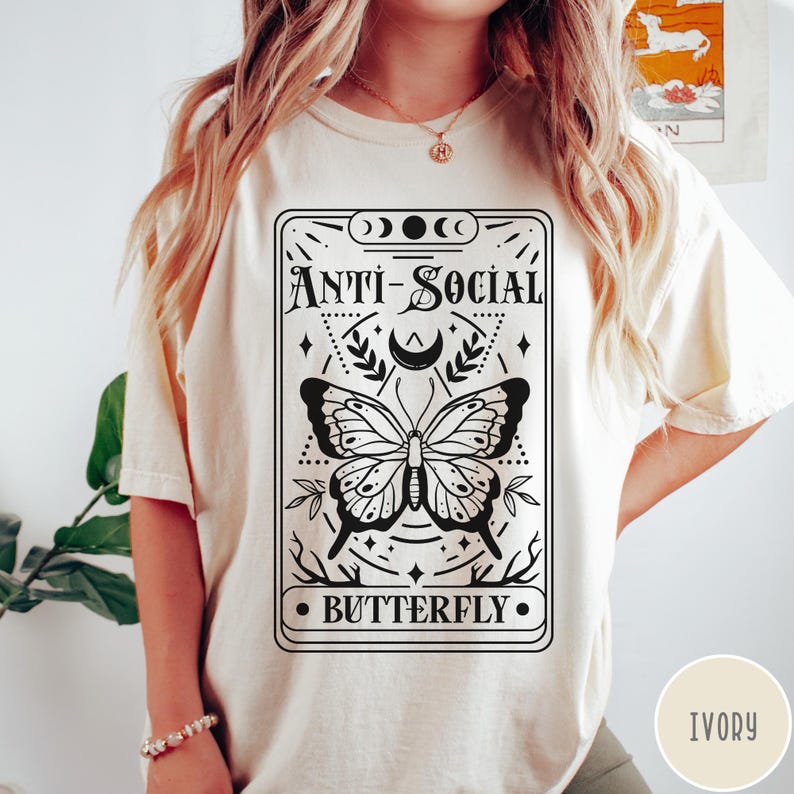 Puede incluir: Una camiseta blanca con un dise&ntilde;o gr&aacute;fico en blanco y negro de una mariposa con el texto "Anti-Social Butterfly".