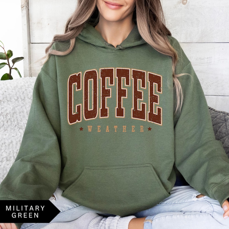 Puede incluir: Una sudadera con capucha verde con el texto "COFFEE WEATHER" en letras marrones.