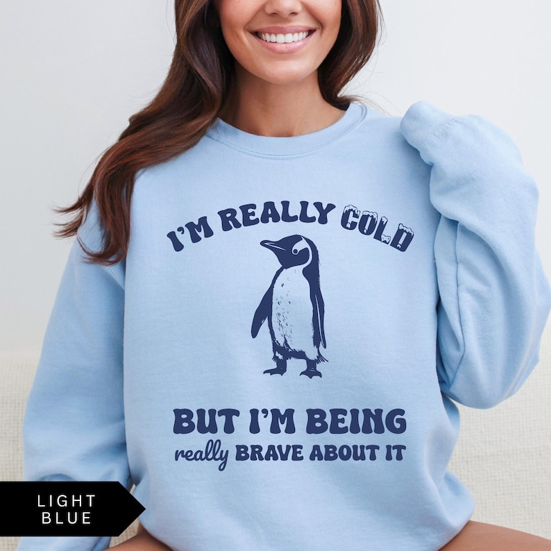 May include: Light blue sweatshirt with a penguin graphic and the text "I'm really cold but I'm being really brave about it."