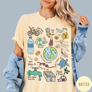 May include: A yellow t-shirt featuring a colourful illustration of various ways to help the environment. The illustration includes a bicycle, a lightbulb, a recycling symbol, a globe, a turtle, a tree, and the words "save the planet".