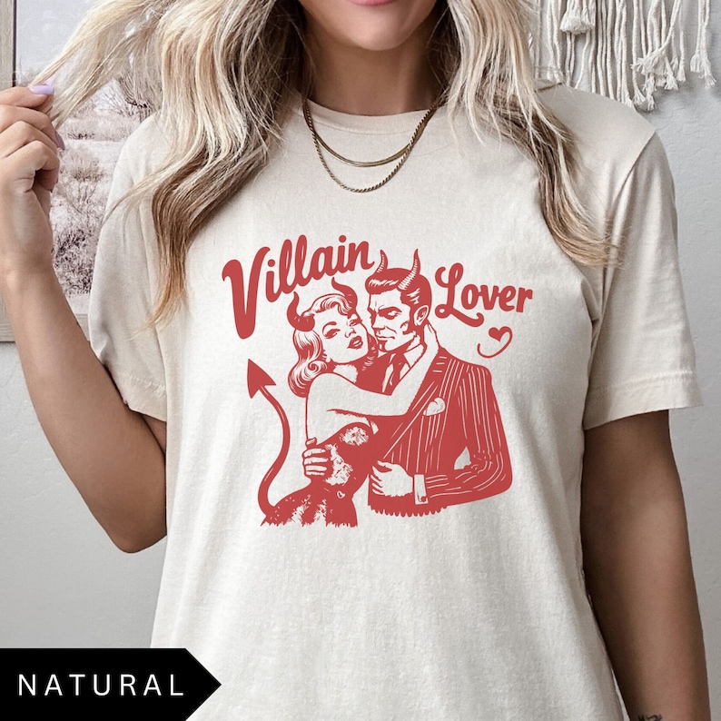 May include: A cream colored t-shirt with a red graphic of a devil couple. The text "Villain Lover" is above the couple.