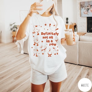 May include: White t-shirt with a graphic of ducks and the text "Definitely not all in a row".