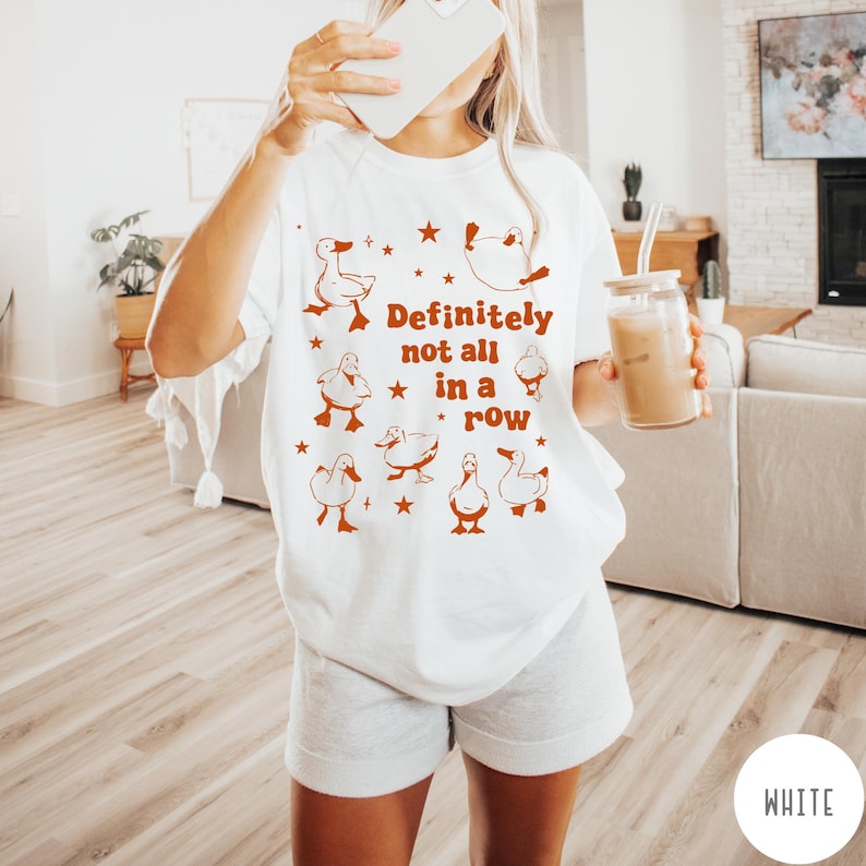 May include: White t-shirt with a graphic of ducks and the text "Definitely not all in a row".