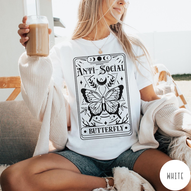Puede incluir: Camiseta blanca con un gr&aacute;fico en blanco y negro de una mariposa y el texto "Anti-Social Butterfly".
