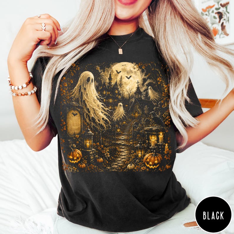 Puede incluir: Una camiseta negra con un estampado gr&aacute;fico detallado de una escena embrujada con fantasmas, luna llena, una mansi&oacute;n oscura, calabazas y linternas. La ilustraci&oacute;n utiliza tonos dorados y marrones c&aacute;lidos para representar el cementerio.