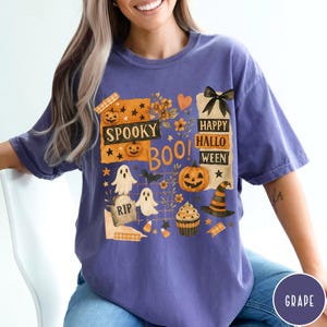 Op de afbeelding: Een paars T-shirt met een Halloween-thema. Het ontwerp bevat pompoenen, geesten, een heksenhoed en de woorden "Spooky Boo!" en "Happy Halloween."