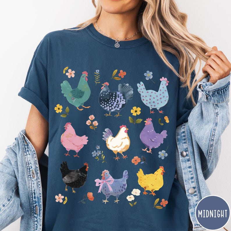 K&ouml;nnte beinhalten: Ein marineblaues T-Shirt mit einem bunten Muster aus H&uuml;hnern und Blumen. Die H&uuml;hner sind alle in verschiedenen Farben und haben unterschiedliche Muster. Die Blumen sind rosa, gelb und lila.