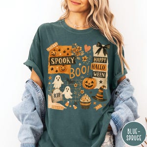 Op de afbeelding: Tealkleurig T-shirt met een Halloween-thema. Het ontwerp bevat pompoenen, geesten, een heksenhoed en de zinnen "Spooky Boo!" en "Happy Halloween". De afbeelding is in oranje, zwart en wit, met bloemen- en steraccenten.