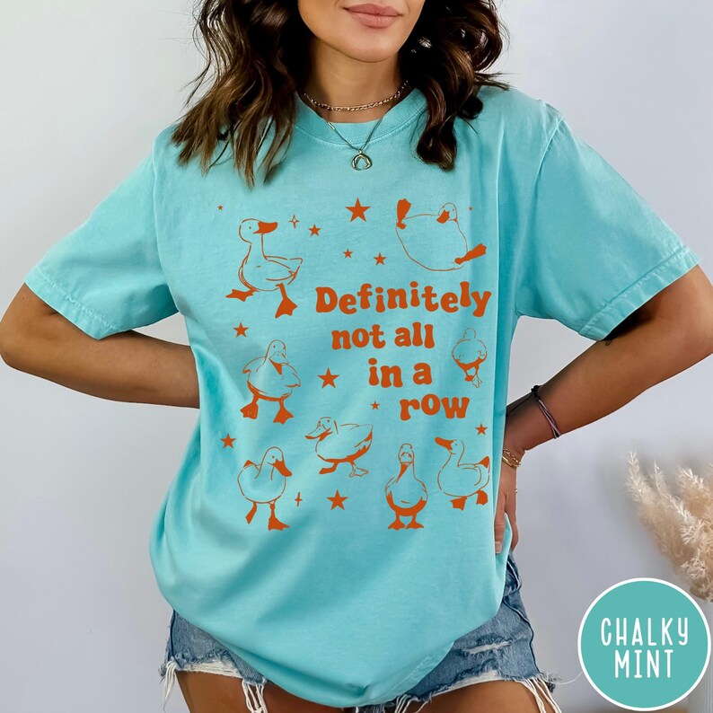May include: A turquoise blue t-shirt with a graphic of ducks in a row and the text "Definitely not all in a row".