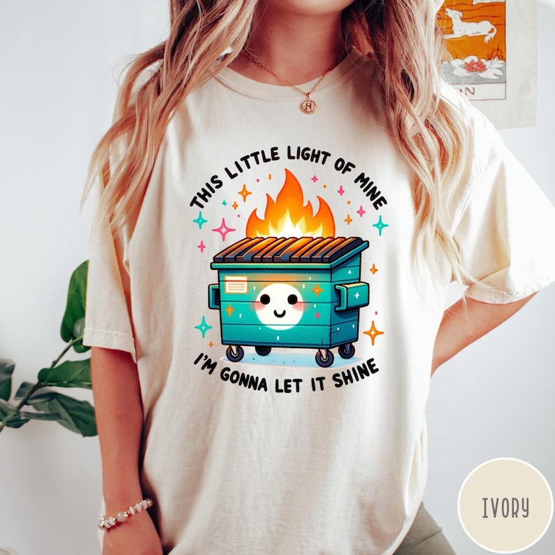 May include: A white t-shirt with a graphic of a green dumpster on fire with the text "This little light of mine, I'm gonna let it shine".