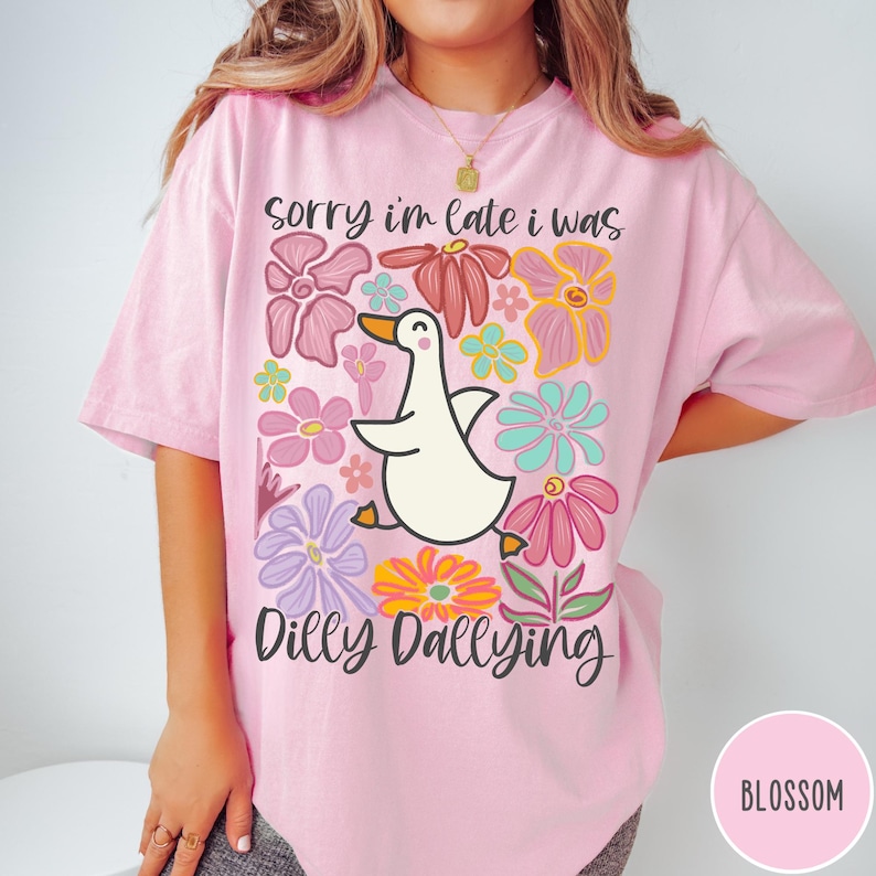 May include: A pink t-shirt with a white duck and colorful flowers. The text on the shirt reads "Sorry I'm late I was dilly dallying".
