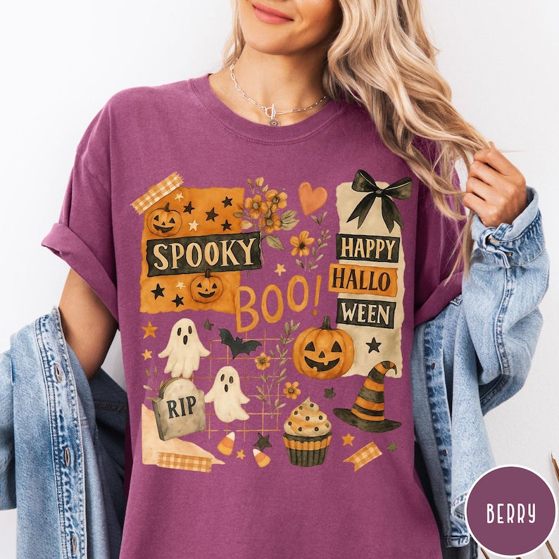 Op de afbeelding: Bessenkleurig T-shirt met een Halloween-thema. Het ontwerp bevat pompoenen, geesten, een heksenhoed en de woorden "Spooky Boo! Happy Halloween." Het shirt heeft korte mouwen en een relaxte pasvorm.