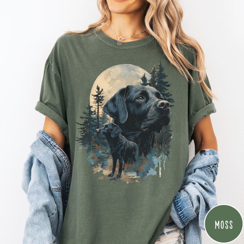 May include: Moss green t-shirt featuring a graphic of a black Labrador Retriever with a full moon and forest background. The design includes two images of the dog, one large and one smaller. The shirt has rolled-up sleeves and a relaxed fit.