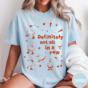 May include: Light blue t-shirt with a graphic of ducks in various poses and the text "Definitely not all in a row".