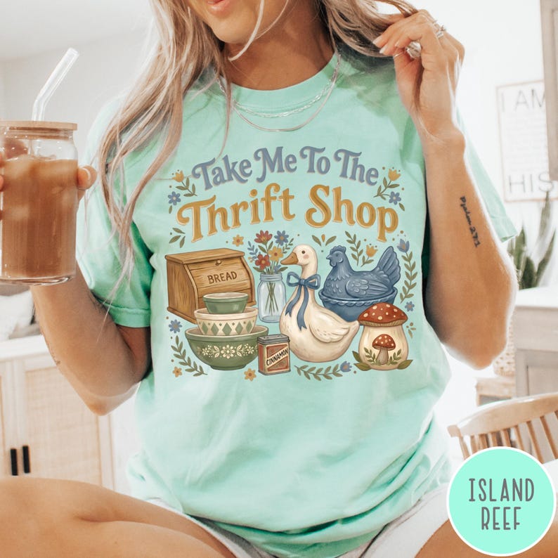 Op de afbeelding: Lichtgroen T-shirt met de tekst "Take Me To The Thrift Shop". De afbeelding bevat een brooddoos, kommen, een eend, een kip en een paddenstoel. Het shirt heeft een comfortabele, casual stijl.