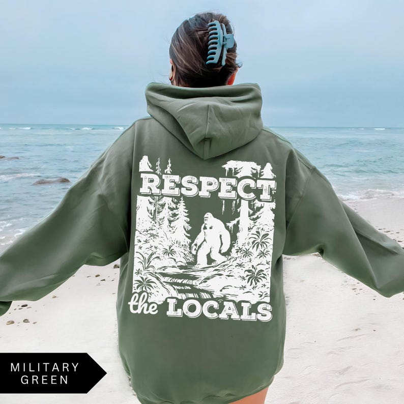 May include: A green hooded sweatshirt with the text "Respect the Locals" in white lettering. The design features a white silhouette of a Bigfoot-like creature in a forest setting.