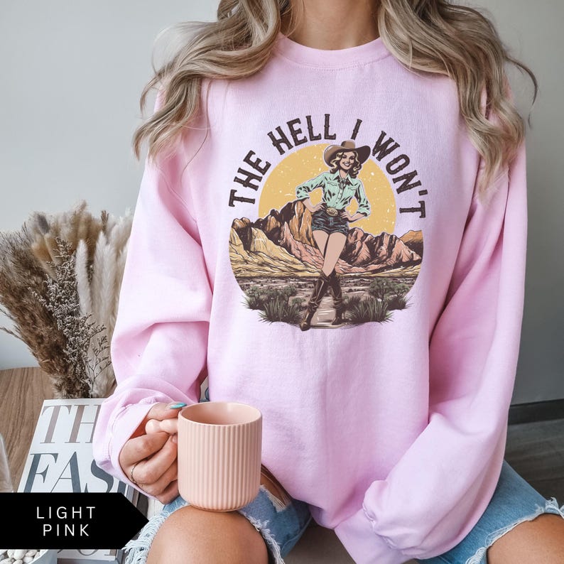 May include: Light pink sweatshirt with a graphic of a woman in a cowboy hat and the text "The Hell I Won't".